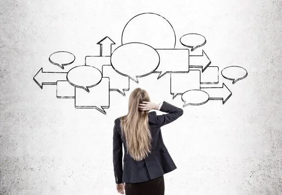 Kobieta stojąca przed ścianą z wieloma pustymi dymkami i strzałkami symbolizującymi decyzje.