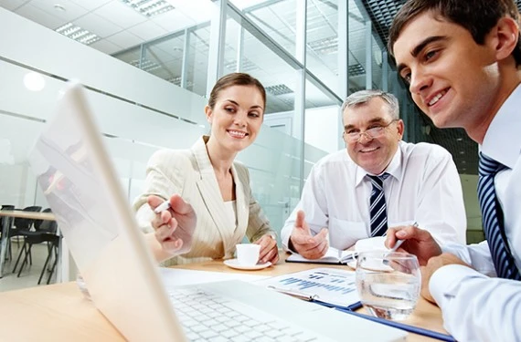 Zadowoleni pracownicy siedzą przy jednym laptopie i omawiają zagadnienie związane z pracą